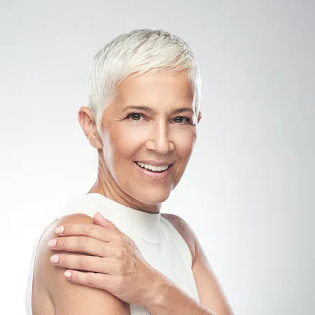 Confident elderly woman with short white hair smiling against a soft white background.