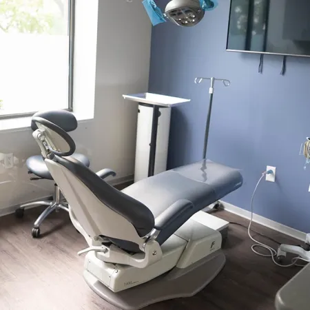 Modern medical examination room with adjustable patient chair, monitor, and medical equipment near window