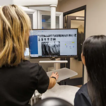 Dentist reviewing dental x-rays on a computer screen with a patient in a dental office setting.