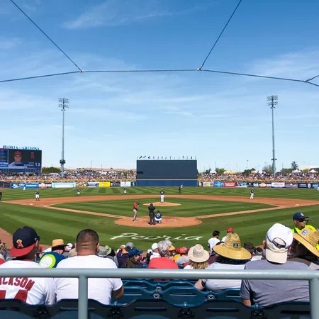 Baseball game in progress with players on field and fans watching from stands under clear blue sky