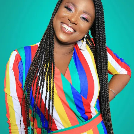 Smiling woman with long braids wearing a colorful striped dress against a teal background