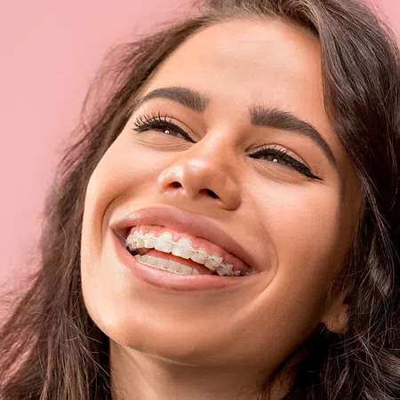 Smiling young woman with braces against a soft pink background, showcasing confidence and joy.