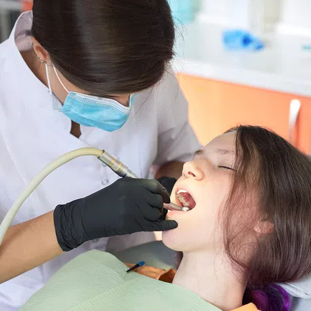 A dentist performing a dental procedure on a young girl in a clinical setting.