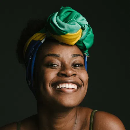 Smiling woman with a colorful headscarf against a dark background, radiating joy and confidence.