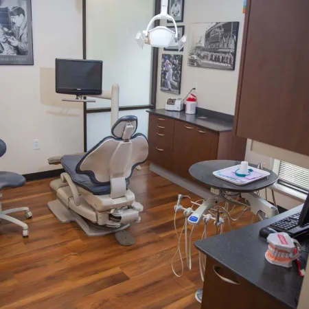 Modern dental office featuring a dentist chair, monitor, dental tools, and wooden flooring in a clean room.