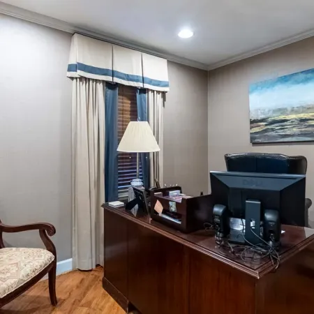 Cozy office space with wooden desk, computer, classic armchair, table lamp, and abstract wall art.