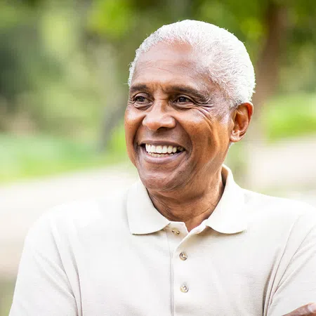 Smiling elderly man outdoors, wearing a light-colored polo shirt, embracing nature.