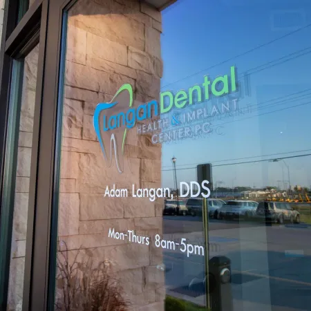 Glass door with Langan Dental Health & Implant Center logo, Adam Langan DDS, and office hours displayed.