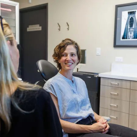 Woman smiling and talking to a healthcare professional in a modern medical office with computer screens and cabinets.