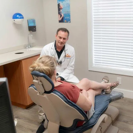 Dentist in white coat consulting with female patient seated in dental chair in bright clinic room