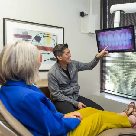 Dentist explaining dental x-ray images on screen to a seated female patient in a modern dental office.
