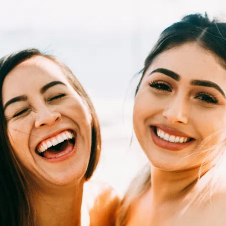 Two young women smiling and laughing outdoors, close-up portrait capturing joy and friendship.