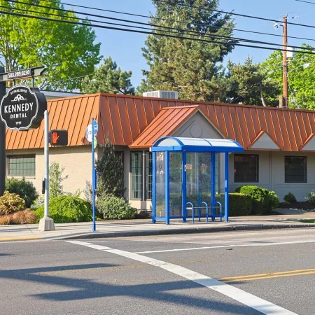 Kennedy Dental office building with orange roof and blue bus stop shelter on sunny day.
