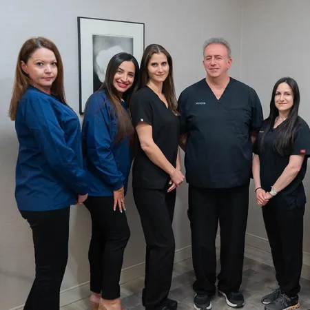 Medical team of seven professionals in scrubs standing in a clinic room with framed art on walls.