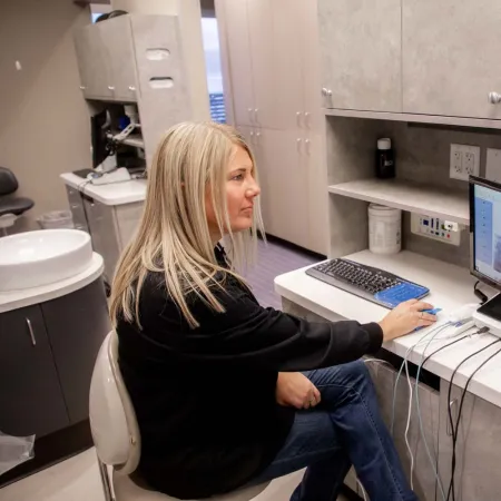 Woman sitting at dental office desk analyzing digital dental X-rays on a computer screen