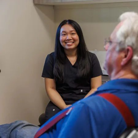 Smiling female healthcare professional talking to an elderly male patient in a clinical office setting.