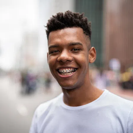 Smiling young man with braces, wearing a white shirt in an urban setting with blurred background.