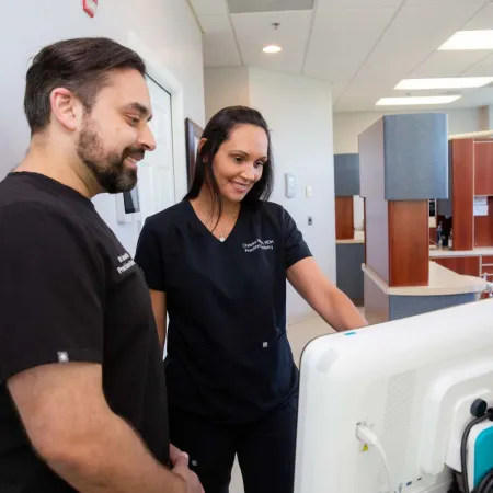 Two dental professionals in black scrubs reviewing information on a computer screen in a dental office.