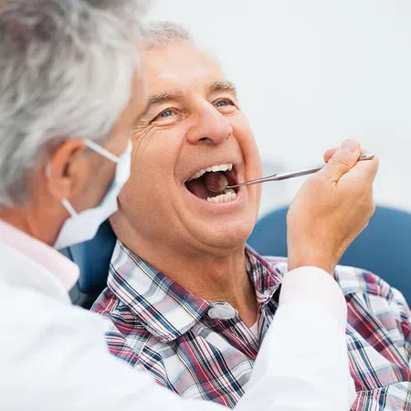 Dentist performing an oral check-up on a smiling senior man in a dental clinic.
