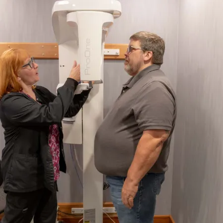 Technician adjusting a ProOne dental imaging machine as a man stands ready for a scan in a clinic room