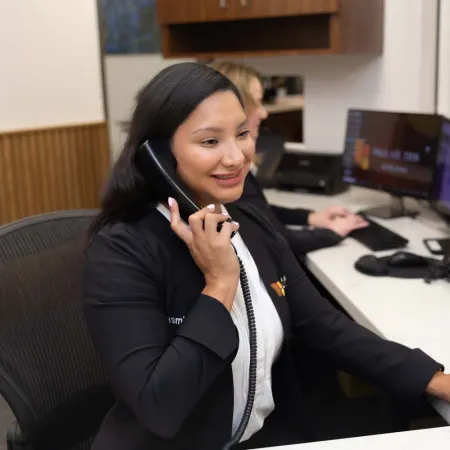 Female receptionist smiling while talking on the phone at a modern office desk with computer screens