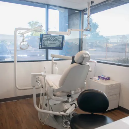 Modern dental clinic room with a patient chair, X-ray monitor, dental tools, and large windows with natural light.