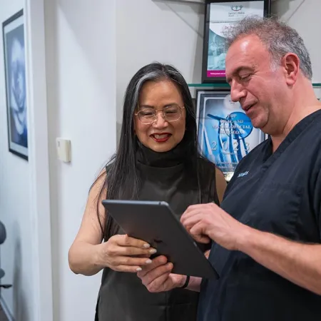 Dentist showing a middle-aged female patient information on a tablet in a dental office setting.
