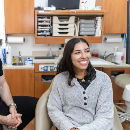 Male dentist in black scrubs and female patient smiling together in a dental office consultation.