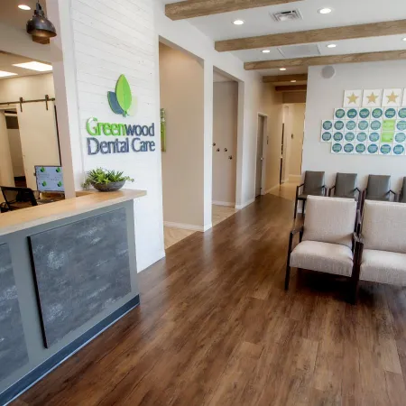 Bright dental office reception and waiting area with wooden floors, chairs, and a Greenwood Dental Care sign.