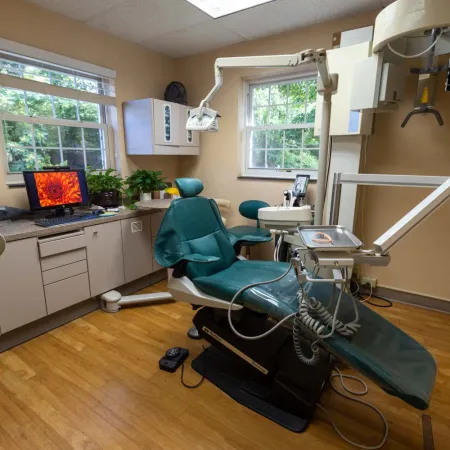 Modern dental office with green dental chair, equipment, computer, and natural light from windows.
