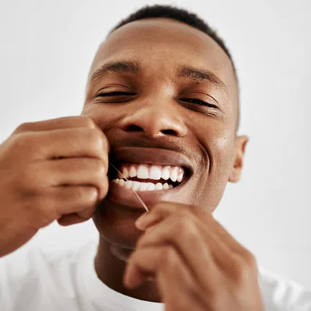 Smiling man using dental floss to maintain oral hygiene and healthy teeth.