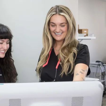 Two female dental professionals smiling and reviewing information on a computer screen in a clinic.