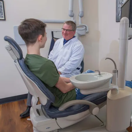 Dentist in white coat consulting with a young male patient sitting in dental chair in clinic room