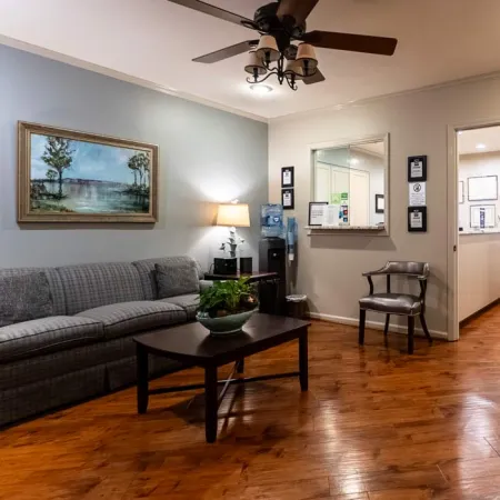 Cozy waiting room with gray couch, wooden coffee table, plants, water dispenser, and hardwood floors