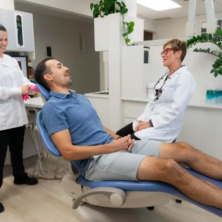 Male patient sitting on dental chair smiling with dentist and assistant in a modern clinic setting