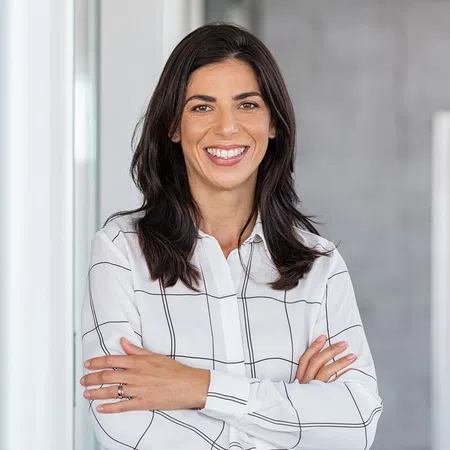 Confident businesswoman smiling with arms crossed in a modern office setting.