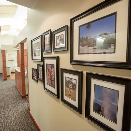Indoor hallway with framed photos on beige walls and carpeted floor leading to open office spaces.