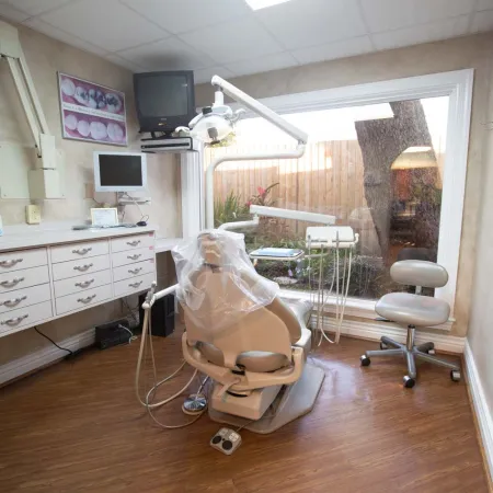 Bright dental office with patient chair, equipment, large window, wood flooring, and cabinetry with monitors.