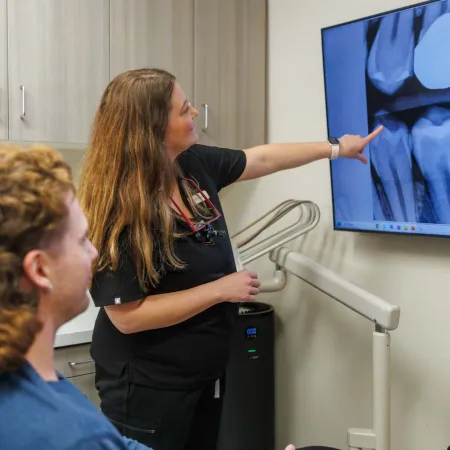 Dentist explaining dental X-ray results to patient showing teeth and roots on a monitor in clinic.