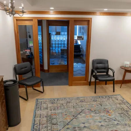 Waiting room with wooden doors, black chairs, patterned rug, wooden desk, and soft overhead lighting.