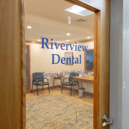 Glass door with Riverview Dental logo opens to a waiting room with chairs and a patterned rug inside the dental office.