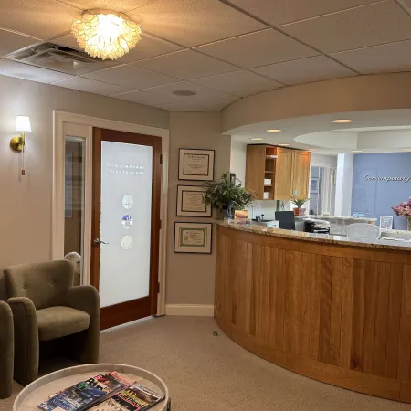 Modern dental office reception area with wooden desk, comfortable chairs, and framed certificates on the wall.