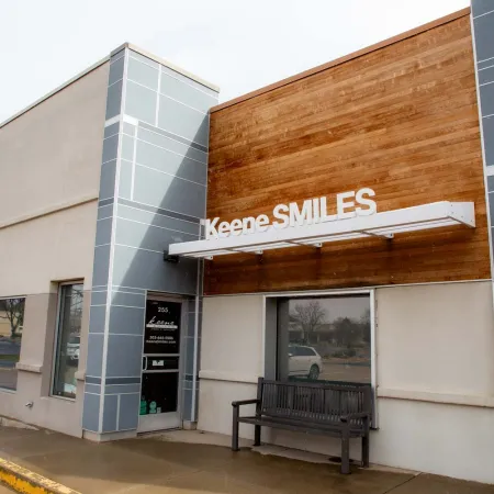 Modern dental office exterior with wood paneling, large windows, and a bench outside Keene SMILES clinic.