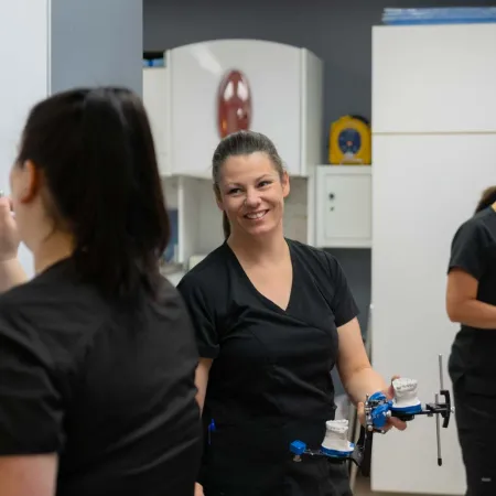Three dental technicians in black scrubs working on dental molds and equipment in a modern dental lab.