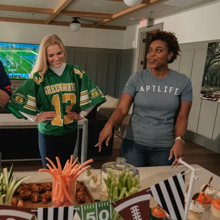 Three friends enjoy football snacks and veggies while watching a game in a cozy living room setting.