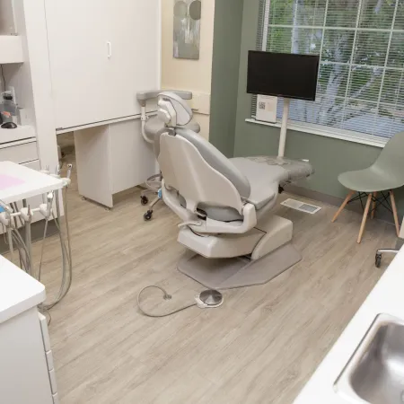 Modern dental clinic room with dental chair, equipment, sink, and window with blinds, bright and clean space