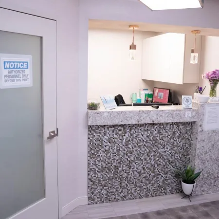 Modern reception area with mosaic tile counter, white cabinets, potted plants, and a frosted door with authorized personnel sign