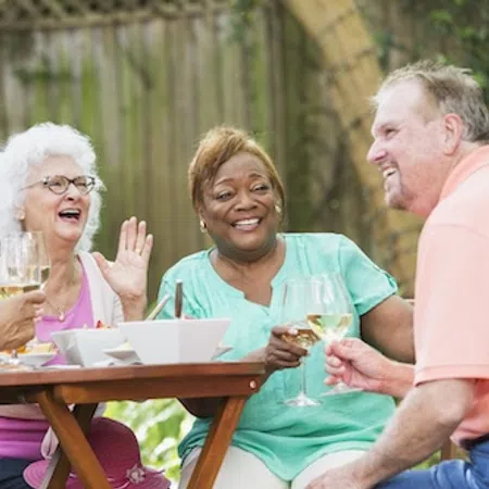 Four diverse seniors happily dining outdoors, enjoying wine and conversation around a wooden table.