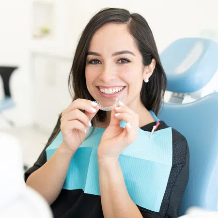 Smiling woman in a dental chair holding clear aligners during a dental appointment.