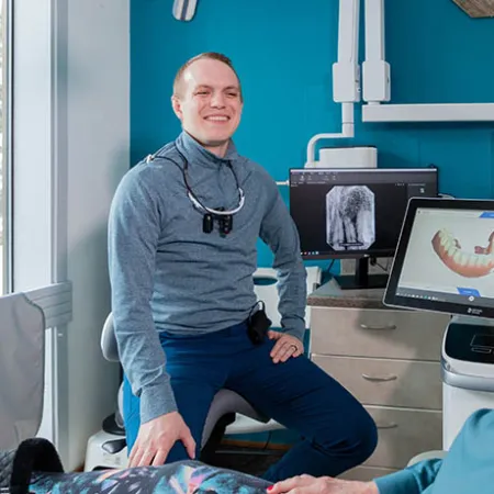 Dentist reviewing dental scans on computer while chatting with smiling elderly female patient in clinic